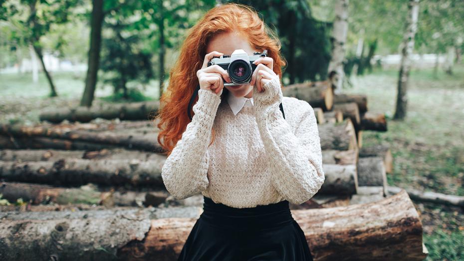 Kobieta z aparatem w lesie  poszukuje inspiracji na zdjęcia w plenerze.