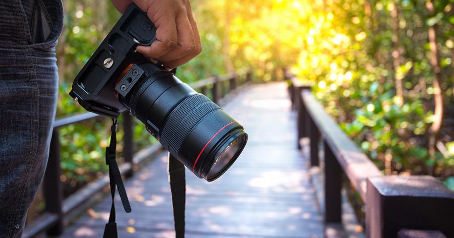 Dłoń trzymająca aparat fotograficzny z mostkiem w tle
